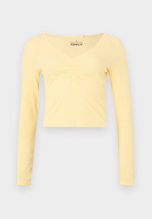 Μπλούζα cropped με μακριά μανίκια σε απαλό κίτρινο ριμπ ύφασμα με λαιμόκοψη σε σχήμα V και ρέλιασμα στο κέντρο μπροστά.