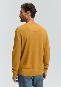 Suéter de punto amarillo mostaza con mangas largas, puños y dobladillo acanalados, y un cuello redondeado; combinado con jeans de mezclilla azul.