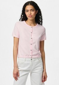 Kortärmad, rosa kofta med rund halsringning och stängning med sju silverknappar. Tillverkad av mjukt material, med en kortad längd.