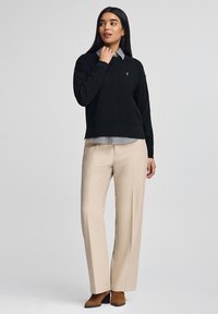 Czarny sweter nałożony na jasną koszulę w kratę, połączony z beżowymi spodniami. Sweter ma okrągły dekolt i ribbowe mankiety.