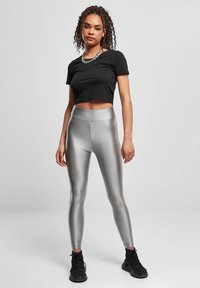 Colanți argintii cu textură netedă și lucioasă, combinați cu un crop top negru cu mâneci scurte și pantofi sport negri. Design simplu, croială mulată.