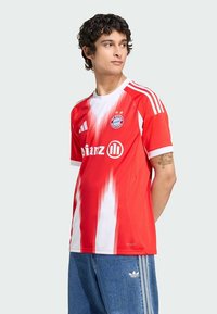 Raudona marškinėliai su balta gradientine spalva ir juostelėmis, puošta FC Bayern Miuncheno logotipu ir rėmėjo ženklu. Trumpomis rankovėmis, lengvos medžiagos, sportiško stiliaus.