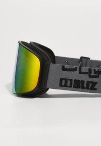 Gogle narciarskie z dużą, odbijającą żółto-zieloną soczewką, miękką czarną ramką z pianki oraz szarym paskiem z czarnym logotypem "BLIZ".