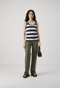 Marineblå og hvite stripete tanktop kombinert med olivengrønne cargo-bukser. Modellen holder en liten svart håndveske og har på seg svarte sandaler med nagler.