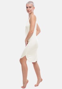 Abito senza maniche di colore crema chiaro, con design aderente, texture morbida e spacchi laterali per una maggiore libertà di movimento, lunghezza al ginocchio e un leggero splendore.