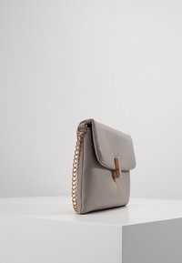 Šedá kožená kabelka se zavíráním na klopu, zlatým řetízkovým popruhem a obdélníkovým zlatým detailem na přední straně. Texturovaný povrch.