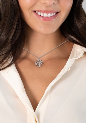 Collana a catena con pendente a forma di albero della vita in argento, caratterizzata da foglie e rami intagliati in modo intricato, indossata sopra una blusa di colore chiaro.