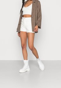 Vita stridskängor med en kraftig sula och snörningsdetaljer. Bärs med vita shorts och en mönstrad brun rutigt blazer över en kort topp.