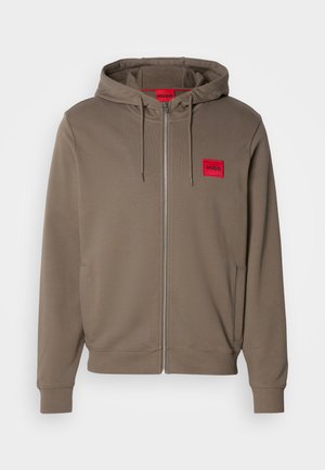 Hugo Kapuzenjacke in Taupe, mit rotem Etikett auf der linken Brust, Kordelzug-Kapuze und gerippten Bündchen. Glattes Material und lockere Passform.