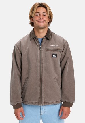 Brown zip-up jacket with a collar, side pockets, and a chest pocket. Features a logo patch and ribbed cuffs and hem.
