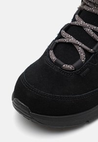 Crne nubuk tenisice s teksturiranom površinom, s reflektirajućim tamnosivim vezicama provučenim kroz ojačane petlje i izdržljivim gumiranim potplatom.