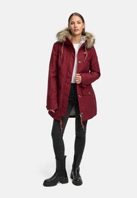 Burgundowy park z futrzanym wykończeniem, kaptur na sznurku, zapięcie na guziki i zamek, dwie przednie kieszenie, w połączeniu z czarnymi obcisłymi dżinsami i botkami.