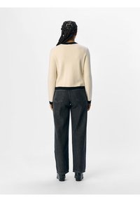 Ljuskrämfärgad tröja med svart nederkant och manschetter, kombinerad med högmidjade, löst sittande mörka jeans. Slät textur och minimal detaljering.