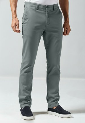 Lichtgrijze slim-fit broek met knoopsluiting, platte voorkant en een gladde textuur. Gecombineerd met donkerblauwe instapschoenen.