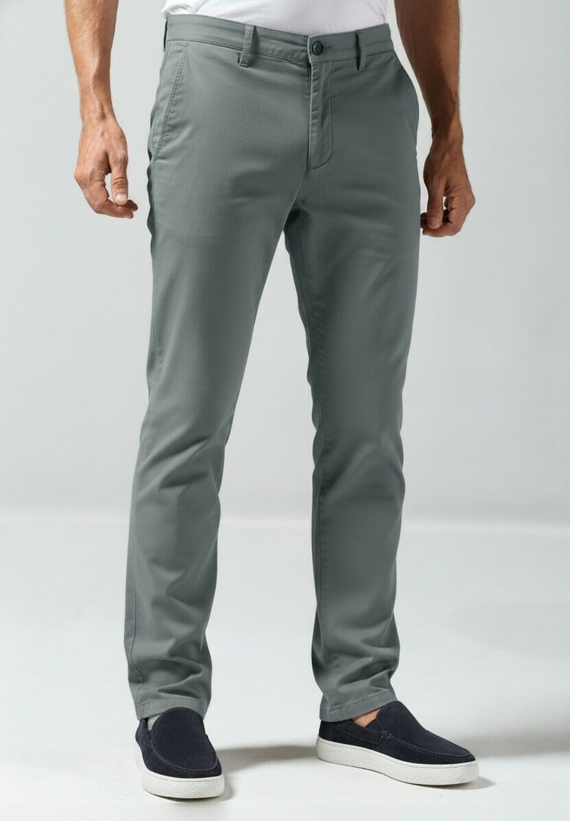 Lichtgrijze slim-fit broek met knoopsluiting, platte voorkant en een gladde textuur. Gecombineerd met donkerblauwe instapschoenen.