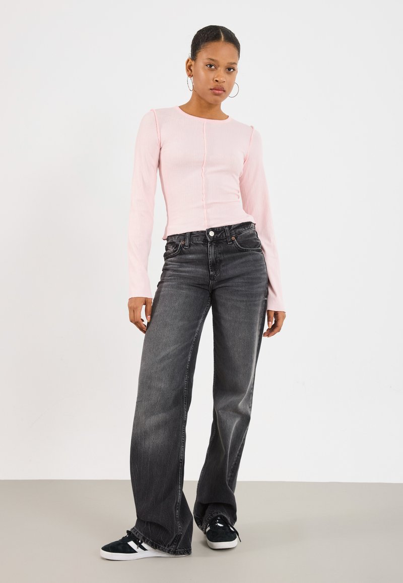 Lyserød ribbet langærmet bluse med knapper foran, parret med høj talje sorte vide jeans og sorte sneakers med hvide detaljer.
