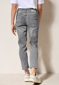 Pantalones de mezclilla gris con corte recto, que cuentan con dos bolsillos traseros y marcas de desgaste sutiles. Combinados con zapatillas deportivas de color claro.