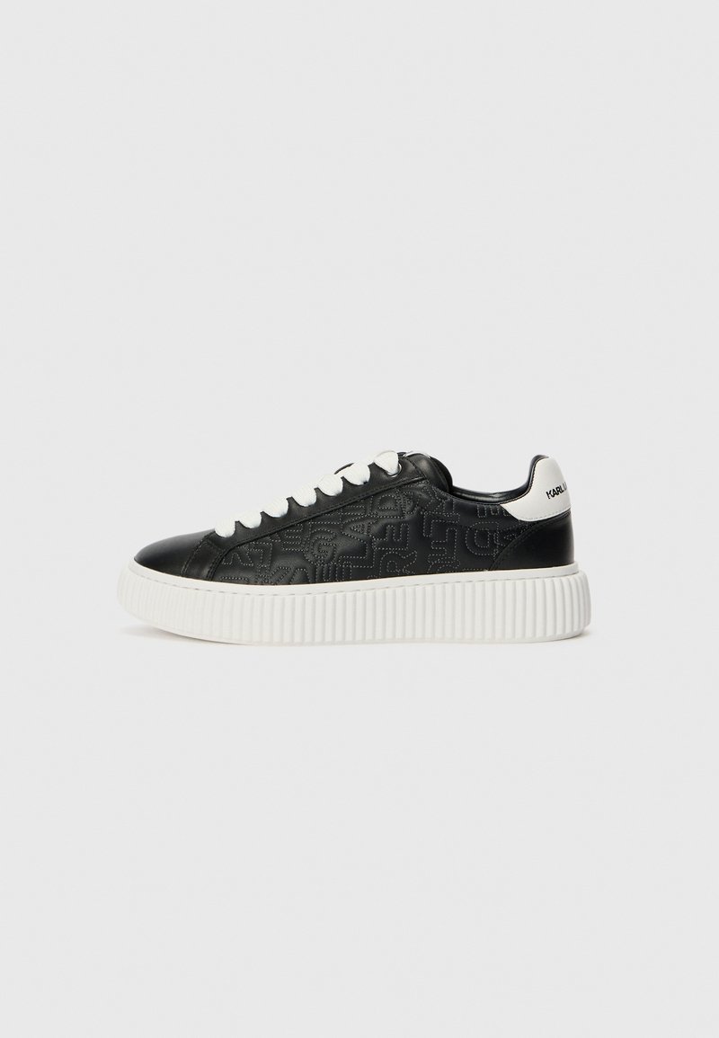 Fekete bőr sneaker dombornyomott mintával, fehér textúrájú talppal és fehér fűzőkkel. Márkanevének kiemelése fehér színben a sarokon.