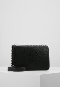 Borsa nera con esterno testurizzato a motivo rettile. Presenta una tracolla a catena argentata e un design piatto per un trasporto facile.