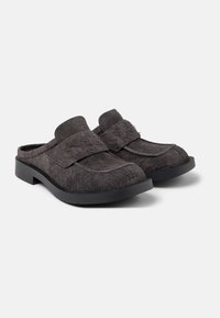 Zuecos forrados de piel negra con una amplia correa en el empeine, suela de goma plana y punta redonda, con una superficie texturizada.