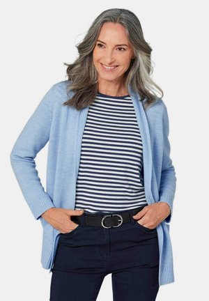 Cardigan bleu clair avec devant ouvert, poignets côtelés. Chemise rayée bleu marine et blanche en dessous, accompagnée de pantalons sombres et d'une ceinture noire.