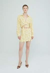 Geel en wit gestippeld crop top met lange mouwen en uitsnijdetails, gecombineerd met een bijpassende mini-jurk. Bruine hoge hakken.