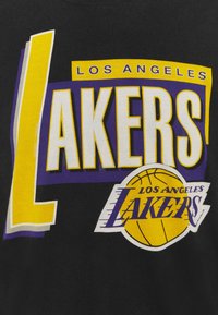 T-shirt nera con una grafica vivace e ampia dei "Los Angeles Lakers" in giallo e viola, completa di icona del basket e lettering stilizzato.