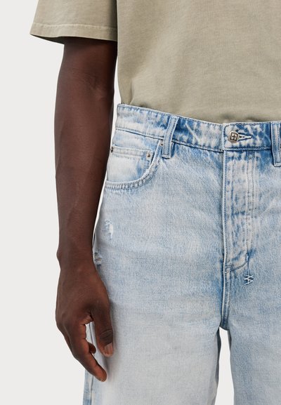 Calças de ganga em denim azul claro desgastadas, com fecho de botão e um leve desbotado. O tecido apresenta vários detalhes envelhecidos e um corte solto.