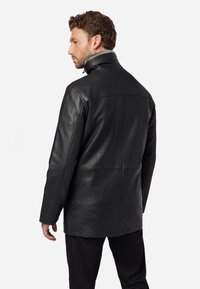 Schwarze Lederjacke mit hohem Kragen und glatter Textur, die sichtbare Nähte und einen geraden Schnitt aufweist, von hinten betrachtet.