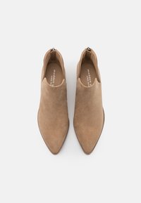Beżowe zamszowe botki za kostkę z wydłużonym noskiem i designem typu slip-on. Posiadają mały zamek z tyłu oraz płaską podeszwę. Gładka tekstura na całej powierzchni.