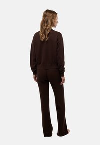 Pull à côtes marron et pantalon assorti, fabriqués en tissu doux. Le pull a une coupe décontractée avec des poignets ; le pantalon est évasé en bas.