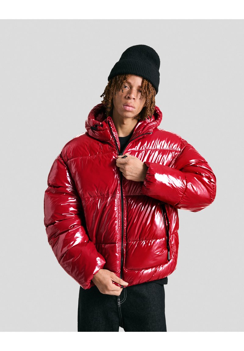 Giacca puffer rossa con finitura lucida, chiusura con zip, cappuccio e vestibilità oversize. Presenta sezioni trapuntate e tasche laterali.