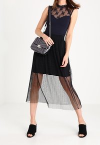 Gonna nera plissettata con sovrapposizione trasparente, abbinata a un top blu navy con pizzo floreale e scollo arricciato. Accessoriata con una borsa metallica.