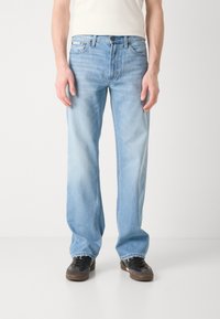 Ljust blå rakbenade jeans med blekta partier, femfickorsdesign och knappstängning. Bärs med svarta skor.