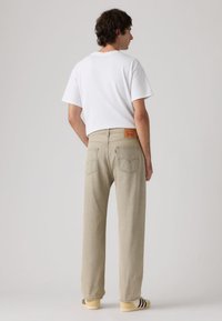 Ελαφρώς μπεζ τζιν παντελόνι με ευρεία γραμμή, ξεθωριασμένη υφή, κόκκινο δερμάτινο ταμπελάκι της επωνυμίας στο πίσω μέρος και ψηλή μέση, συνδυασμένο με λευκό μπλουζάκι.