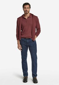 Burgundy långärmad pikétröja under en matchande tröja, tillsammans med blå denimjeans och svarta skor med bruna snören.