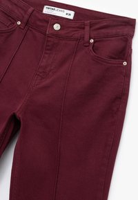 Bordeauxfarvede jeans lavet af bomuld med en tekstureret overflade. Har fem lommer, en lynlås i gylpen og hardware i sølvtonet på størrelsen.