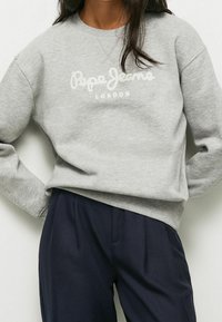 Sudadera gris hecha de material suave con un logo blanco que dice "Pepe Jeans London". Puños y dobladillo acanalados con un ajuste holgado.