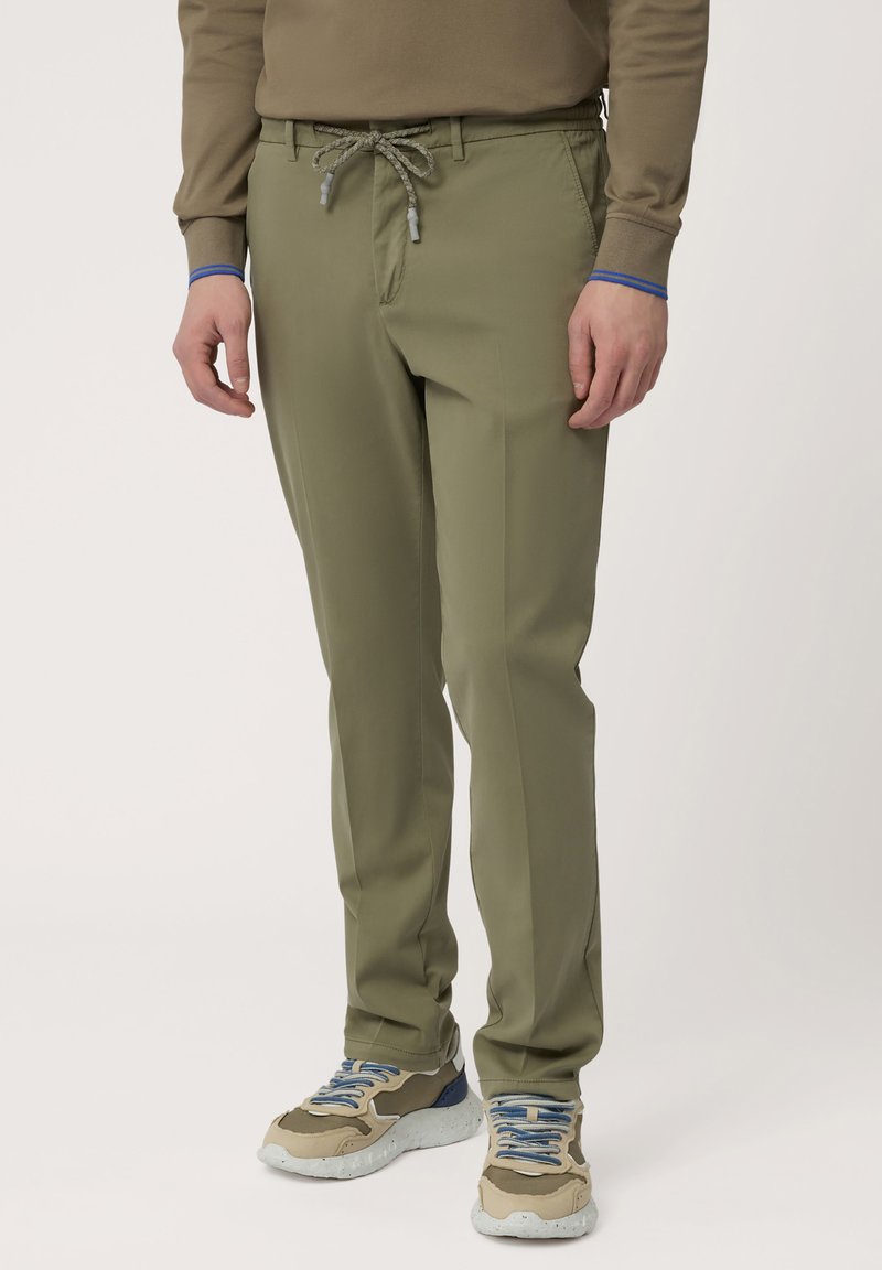 Pantalones verde oliva con cintura elástica, piernas ajustadas y bolsillos laterales. Combinados con zapatillas beige y gris con acentos azules.