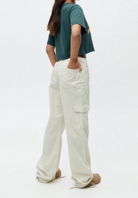 T-shirt vert raccourci avec un motif graphique, associé à un pantalon cargo ample de couleur crème avec des poches et un tissu texturé.