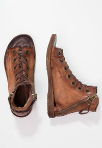 Hnědé kožené kotníkové boty s šněrováním vpředu, bočním zipem a opotřebovanou texturou. Design má zaoblenou špičku a odhalené švy.