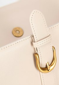 Borsa tote in pelle beige con accessori in tonalità oro, dettagli cuciti e chiusura a scatto circolare. Finitura liscia e morbida.