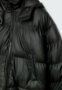 Veste matelassée noire avec une texture lisse et brillante, coutures horizontales, fermeture éclair et une poche plaquée à l'avant.