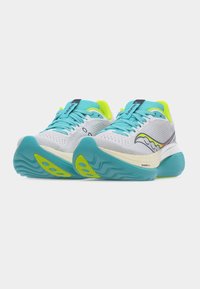 Ζευγάρι λευκά και τιρκουάζ  παπούτσια τρεξίματος με νέον κίτρινες λεπτομέρειες και υφή στις σόλες, παρουσιάζονται σε απλό φωτεινό φόντο.