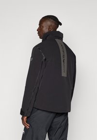 Schwarze Jacke mit hohem Kragen und strukturiertem Rückenteil. Besticht durch ein klares Design, verstärkte Nähte und subtile Logo-Akzente.