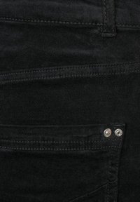 Sorte denim jeans med en glat tekstur, med to metalliske knapper på frontlommen og synlige syninger langs kanterne.