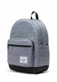 Sac à dos en tissu gris avec dessus arrondi, fond noir, poche avant zippée et écusson avec logo. Comprend une poignée supérieure et des bretelles réglables.