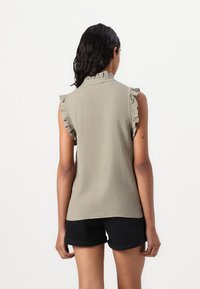 Blusa senza maniche di un verde oliva chiaro con spalline arricciate, colletto alto e un tessuto morbido. Indossata con pantaloncini neri.