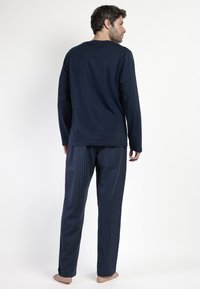 Top de manga larga azul marino combinado con pantalones azul marino a rayas, confeccionados con una tela suave. La prendas tienen un corte relajado y un diseño sencillo.