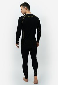 Black thermal long-sleeve top and leggings with contrasting yellow stitching. The fitted design features long sleeves and a rounded hem.